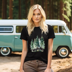 Puede incluir: Una camiseta negra con un dise&ntilde;o de acuarela de un bosque con &aacute;rboles verdes. La camiseta la lleva puesta una persona con el pelo largo y rubio. La persona est&aacute; de pie delante de una furgoneta vintage.