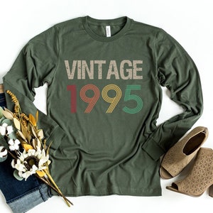 May include: A green long-sleeved t-shirt with the text "Vintage 1995" in a retro font with colorful accents.