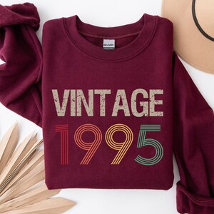 May include: Burgundy sweatshirt with a vintage 1995 design in rainbow colors. The text "Vintage" is above the year.