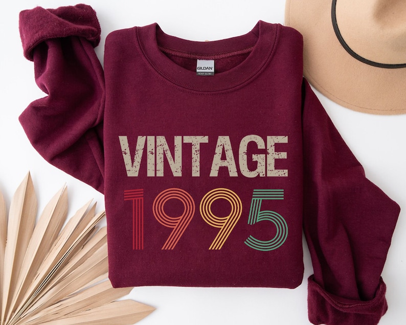 May include: Burgundy sweatshirt with a vintage 1995 design in rainbow colors. The text "Vintage" is above the year.