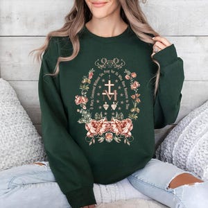 May include: A forest green sweatshirt with a floral design and the text "Pray for Us Who Have Recourse to Thee" in a gold font.