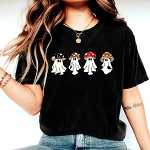 May include: Black t-shirt featuring a graphic of four ghosts wearing mushroom hats. The ghosts are white and the mushrooms are red, brown and black.