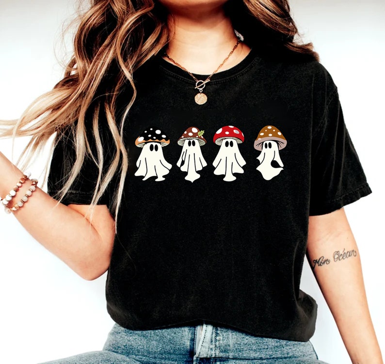 May include: Black t-shirt featuring a graphic of four ghosts wearing mushroom hats. The ghosts are white and the mushrooms are red, brown and black.