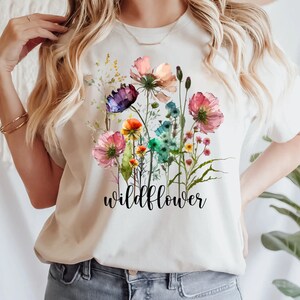 May include: White t-shirt featuring a watercolour design of colourful wildflowers and the word "wildflower" printed in black.