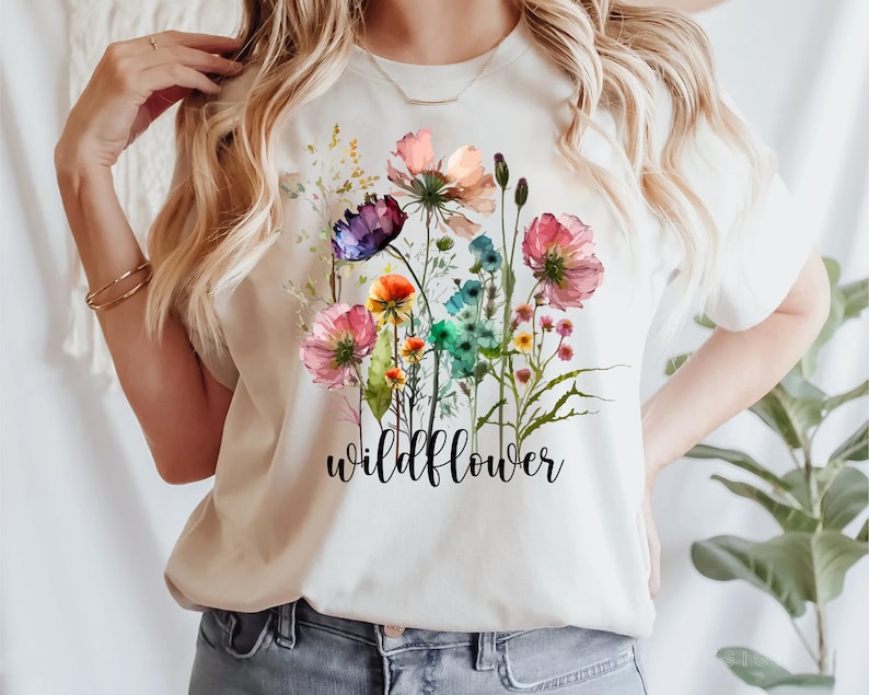 May include: White t-shirt featuring a watercolour design of colourful wildflowers and the word "wildflower" printed in black.