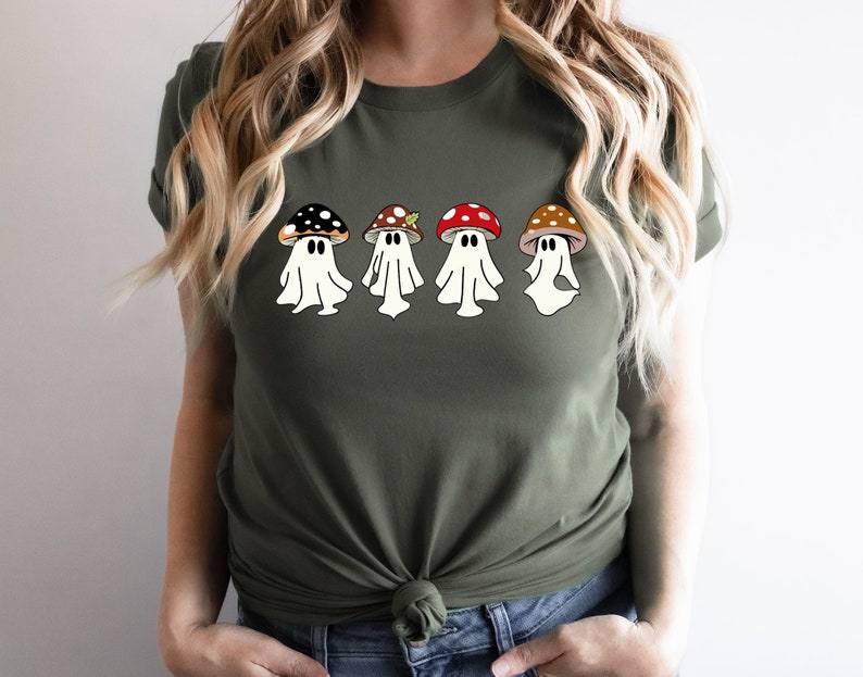 May include: A green t-shirt featuring a design of four ghosts wearing mushroom hats. The mushrooms are red, brown and black with white spots.