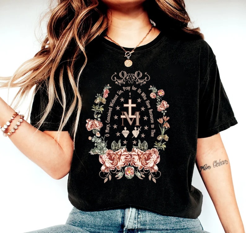 Op de afbeelding: Zwart T-shirt met een bloemenmotief en de tekst "O Maria, ontvangen zonder zonde, bid voor ons die onze toevlucht tot u nemen".