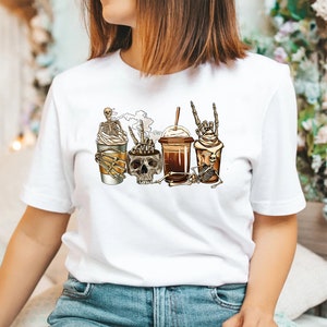 K&ouml;nnte beinhalten: Wei&szlig;es T-Shirt mit einem Aufdruck von vier Kaffeetassen mit Skeletten und Sch&auml;deln. Die Tassen sind mit Schlagsahne bedeckt und haben Strohhalme.