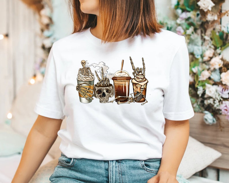K&ouml;nnte beinhalten: Wei&szlig;es T-Shirt mit einem Aufdruck von vier Kaffeetassen mit Skeletten und Sch&auml;deln. Die Tassen sind mit Schlagsahne bedeckt und haben Strohhalme.
