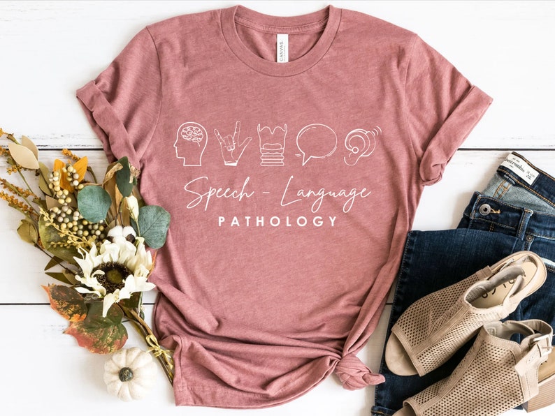 May include: A pink t-shirt with a white graphic design featuring icons related to speech and language pathology. The text "Speech - Language PATHOLOGY" is printed below the icons.