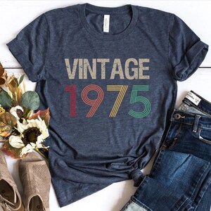 May include: A navy blue t-shirt with a vintage-style graphic that says "Vintage 1975" in red, yellow, and green.