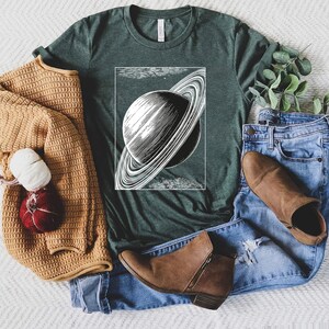 May include: A dark green t-shirt with a vintage illustration of Saturn with its rings. The illustration is in black and white and is centered on the shirt.