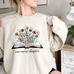 May include: A cream-colored sweatshirt with a graphic of an open book with flowers growing out of it. The text "one more chapter" is printed below the book.