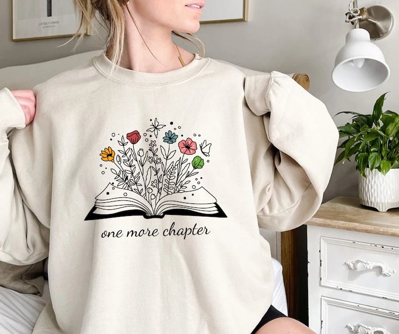 May include: A cream-colored sweatshirt with a graphic of an open book with flowers growing out of it. The text "one more chapter" is printed below the book.