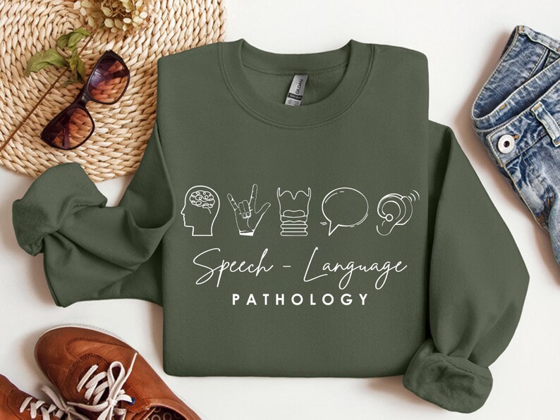 May include: A green sweatshirt with white text that reads "Speech - Language PATHOLOGY". The text is accompanied by five icons representing speech therapy: a brain, a hand making the sign for "I love you", a stack of books, a speech bubble, and an ear.