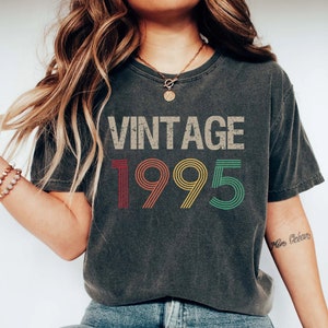 May include: A dark gray t-shirt with the text "Vintage 1995" printed on the front in a colorful, retro font.