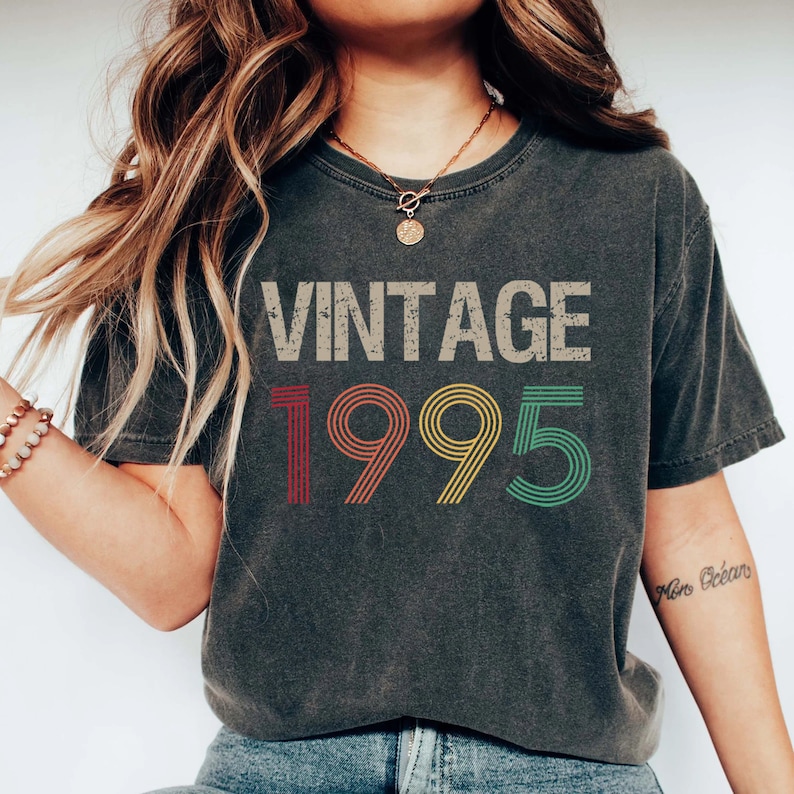 May include: A dark gray t-shirt with the text "Vintage 1995" printed on the front in a colorful, retro font.