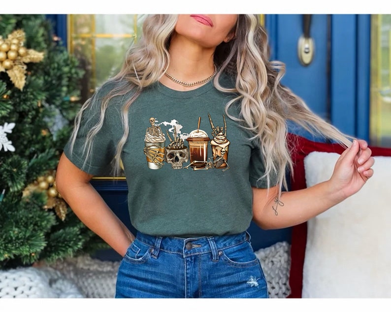 K&ouml;nnte beinhalten: Ein gr&uuml;nes T-Shirt mit einem Aufdruck von vier Kaffeegetr&auml;nken mit Totenk&ouml;pfen und Knochen. Die Getr&auml;nke sind ein Latte, ein Cappuccino, ein Mocha und ein Frappuccino.