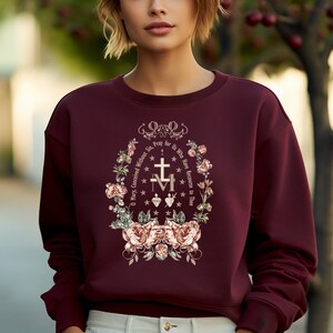 May include: Burgundy sweatshirt with a floral design and the text "O Mary, Conceived Without Sin. Pray for Us Who Have Recourse to Thee" in a gold font.
