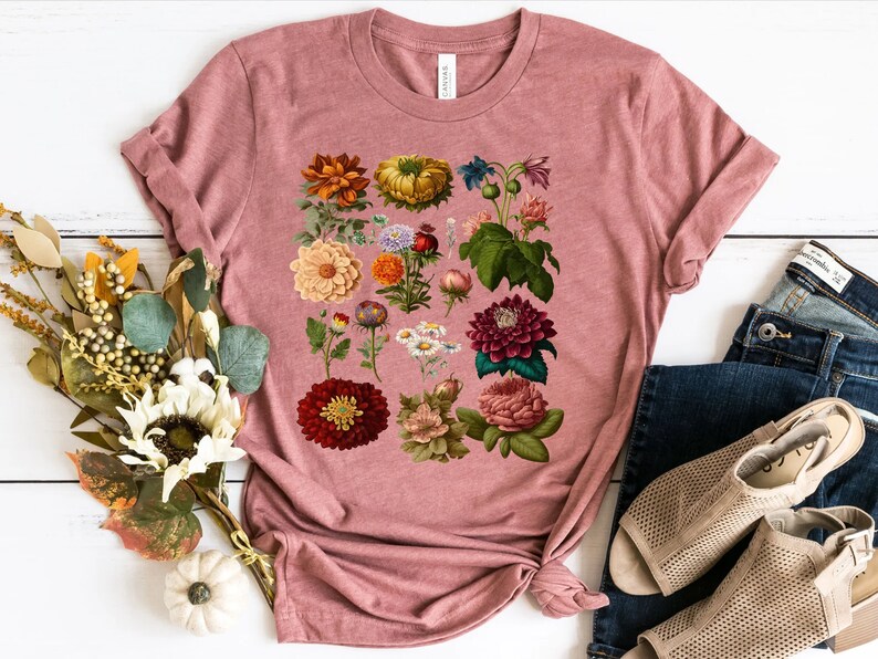 May include: A pink t-shirt with a floral print featuring a variety of flowers in shades of red, pink, yellow, and white.