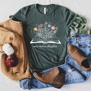 May include: A dark green t-shirt with a white graphic of an open book with flowers growing out of it. The text "one more chapter" is printed below the book.