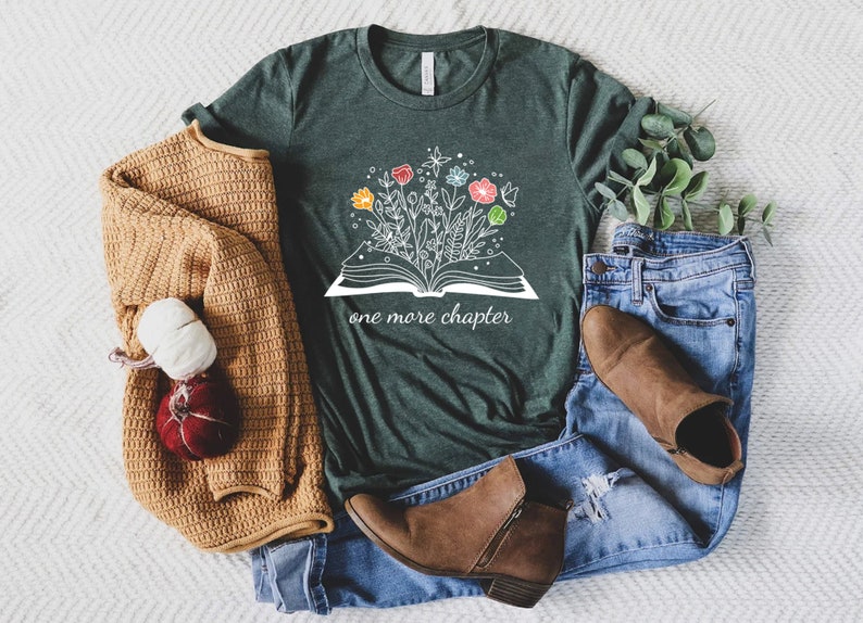May include: A dark green t-shirt with a white graphic of an open book with flowers growing out of it. The text "one more chapter" is printed below the book.