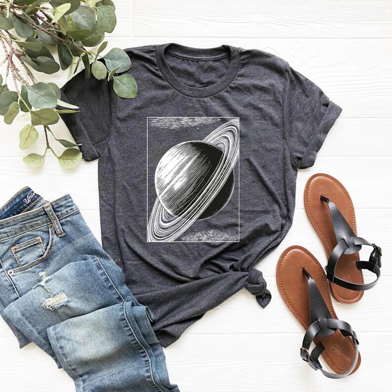 May include: A dark gray t-shirt with a vintage illustration of Saturn with its rings. The illustration is in black and white and is centered on the shirt.
