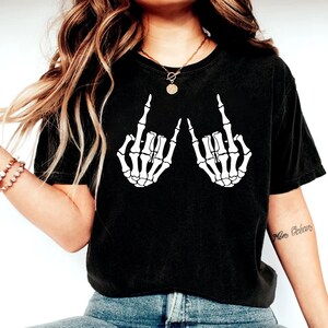 May include: Black t-shirt with a white graphic of two skeleton hands giving the middle finger.