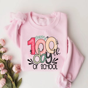 May include: Pink sweatshirt with a graphic design that says "Happy 100th day of school" with colorful numbers and a donut design.