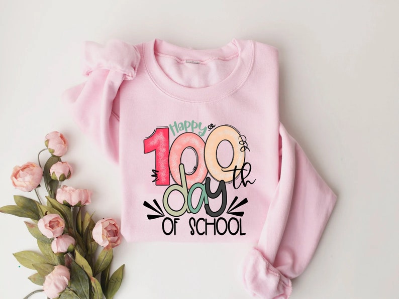 May include: Pink sweatshirt with a graphic design that says "Happy 100th day of school" with colorful numbers and a donut design.