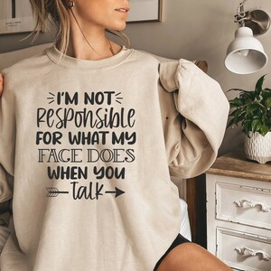 K&ouml;nnte beinhalten: Ein beiger Pullover mit dem Aufdruck "Ich bin nicht verantwortlich f&uuml;r das, was mein Gesicht tut, wenn du sprichst" in Schwarz.