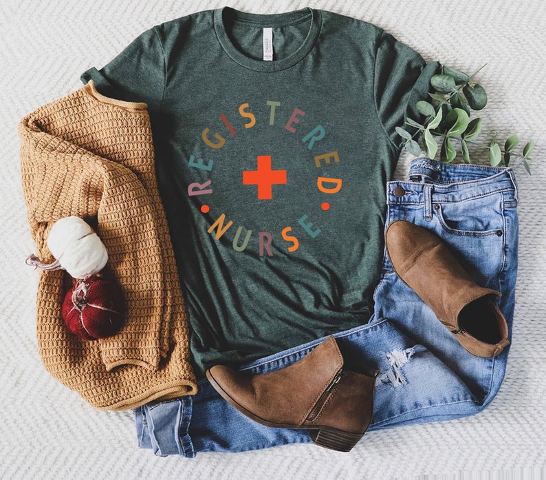 Puede incluir: Una camiseta verde oscuro con un gr&aacute;fico circular de colores que dice "REGISTERED NURSE" con una cruz roja en el centro.