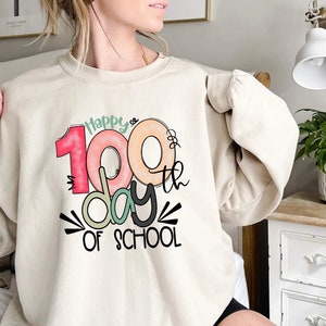 May include: A beige sweatshirt with a graphic design that says "Happy 100th day of school". The number 100 is stylized to look like a donut.