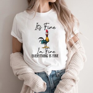 May include: White t-shirt with a cartoon rooster and the text "It's Fine I'm Fine Everything is Fine."