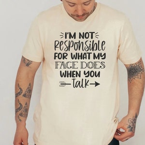 K&ouml;nnte beinhalten: Ein beiges T-Shirt mit einem schwarzen Aufdruck, der "Ich bin nicht verantwortlich f&uuml;r das, was mein Gesicht tut, wenn du sprichst" lautet, mit einem Pfeil, der nach rechts zeigt.