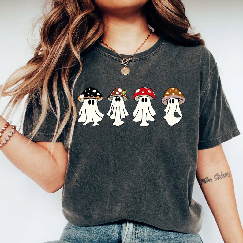 May include: A dark grey t-shirt featuring a graphic of four ghosts wearing mushroom hats. The ghosts are white and the mushrooms are red, brown, and black.