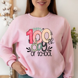 May include: Pink sweatshirt with a graphic design that says "Happy 100th day of school" with colorful donuts forming the number 100.