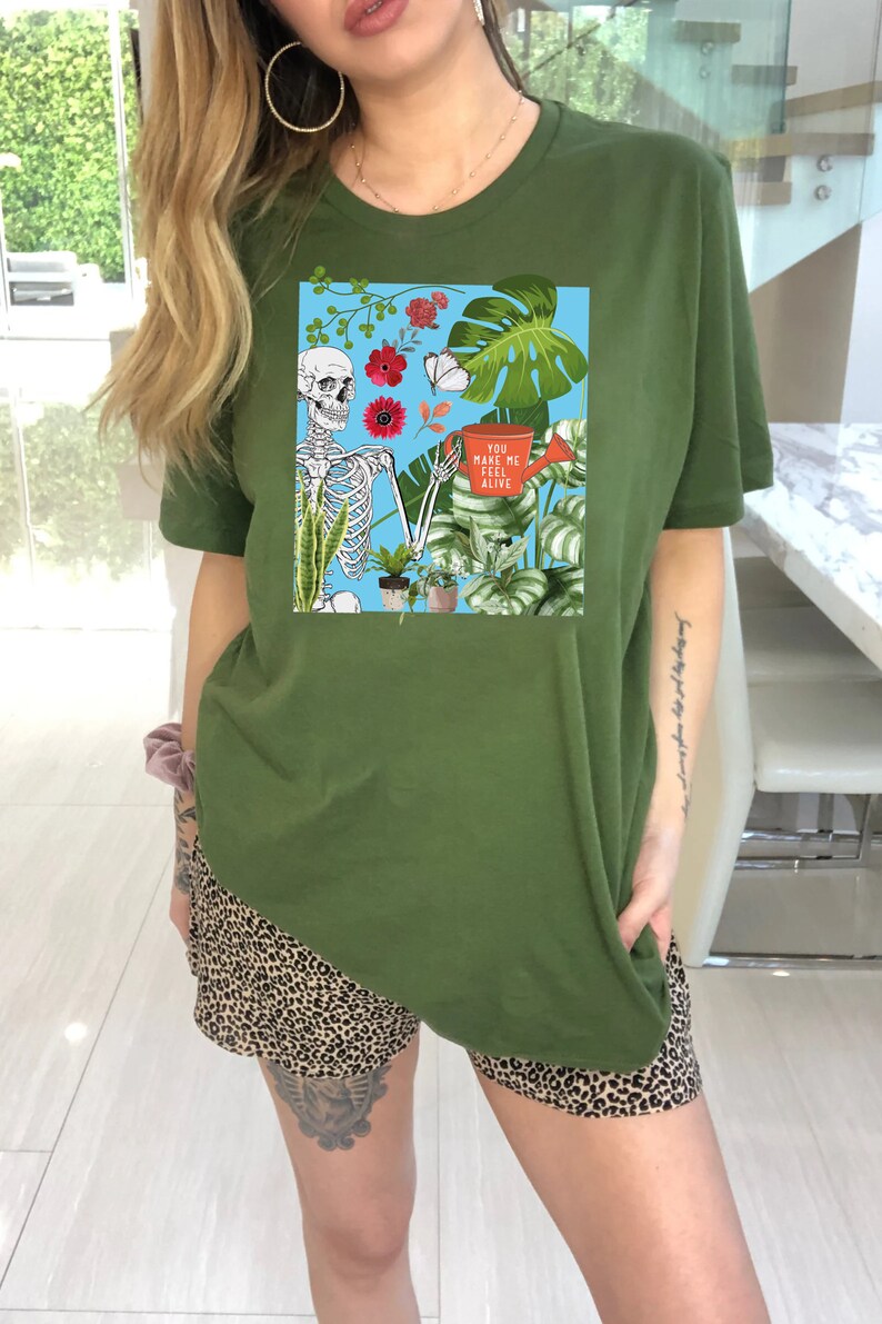 May include: A green t-shirt with a graphic of a skeleton holding a watering can and surrounded by plants. The text on the watering can reads "You make me feel alive".