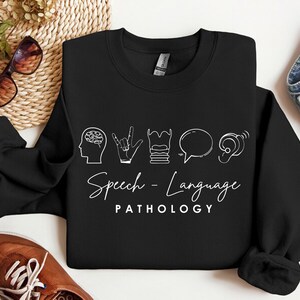 May include: Black sweatshirt with white text and icons that say "Speech-Language Pathology". The icons include a brain, a hand making the sign for "I love you", a stack of books, a speech bubble, and an ear.