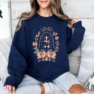 May include: Navy blue sweatshirt with a floral design and the text "O Mary, Conceived Without Sin, Pray for Us Who Have Recourse to Thee" in gold lettering.