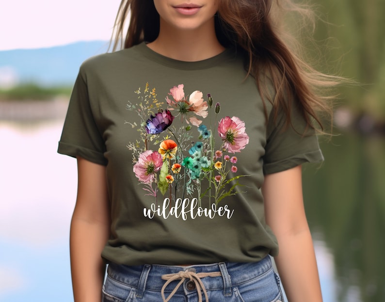 May include: A green t-shirt featuring a watercolour floral design and the word "wildflower" printed in white on the front.