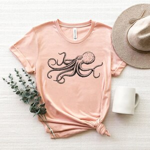 May include: A light pink t-shirt with a black and white illustration of an octopus on the front.