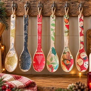Könnte beinhalten: Sechs Holzlöffel hängen an einer rustikalen Holzleiste. Jeder Löffel hat ein einzigartiges weihnachtliches Muster, darunter goldene Sterne, blaue Schneeflocken, rote geometrische Tannen, grüne Stechpalmenblätter, ein Rotkehlchen und Schneemänner.