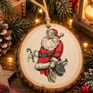 Könnte beinhalten: Ein runder Baumscheiben-Anhänger mit einer Vintage-Illustration vom Weihnachtsmann im roten Anzug, der eine Zuckerstange und einen Spielzeugsack hält. Der Anhänger hat einen natürlichen Rindenrand und ist an einer einfachen Juteschnur befestigt.
