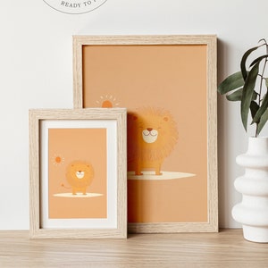 May include: Two framed prints of a cartoon lion with a sun in the background. The prints are on a light brown wooden surface. The larger print is in a light wood frame and the smaller print is in a white wood frame. The background is a white wall with a digital download stamp.
