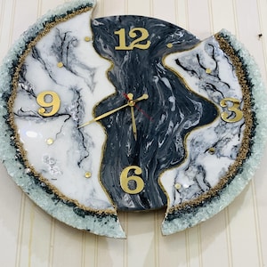 Może przedstawiać: Okrągły, zepsuty zegar z czarno-białym wzorem marmurowym. Tarcza zegara ma złote cyfry i wskazówki. Brzeg zegara jest ozdobiony zielonym i złotym brokatem.