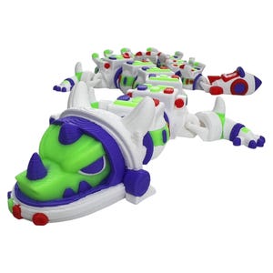 May include: A multi-segmented articulated toy dragon featuring a white, lime green, and purple color scheme. The head has a prominent horn and purple accents, while the long, flexible body consists of several block-like sections with small red, green, and blue circular details. The tail ends in a rocket-shaped tip.