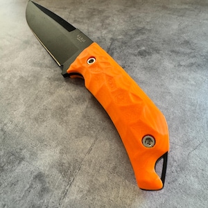 May include: A black blade knife with an orange handle. The knife has a textured handle and a black blade. The brand name "KA-BAR" is visible on the blade. The knife is designed for outdoor use.