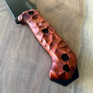 May include: A close-up of a brown wooden knife handle with a textured surface. The handle is attached to a black knife blade with the text "BLACK BEAR GERMANY" on the blade.