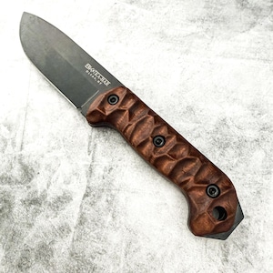 Könnte beinhalten: Ein Messer mit feststehender Klinge, dunkler grauer Klinge und einem braunen, strukturierten Griff. Der Griff ist mit schwarzen Schrauben befestigt. Der Text "BK&T KA-BAR OLEAN, NY" ist auf der Klinge aufgedruckt.
